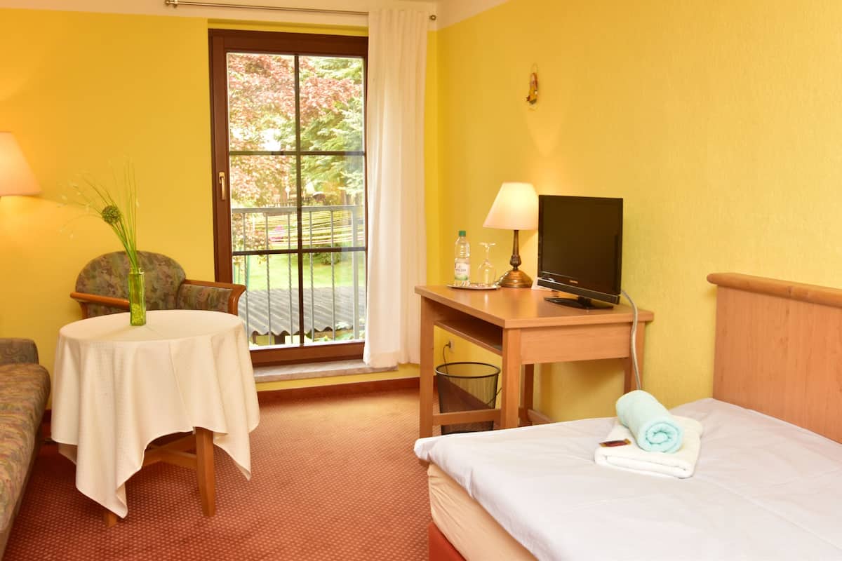 Une chambre d’hôtel avec un lit, une petite table avec une lampe, une chaise, un téléviseur et une fenêtre donnant sur un paysage verdoyant.