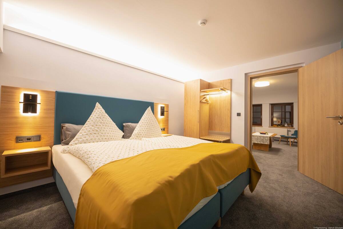 Une chambre d’hôtel moderne, équipée d’un lit, de tables de chevet, d’une armoire et d’une salle de bain visible à travers une porte ouverte.