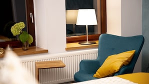 A room with a blue armchair, a yellow pillow, a white lamp, a wooden shelf, and a vase with green flowers. - Landhotel Zur Guten Einkehr (Doberschau-Gaussig)