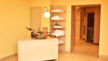 Habitación de hotel con escritorio de madera, un reloj, repisas con toallas y zona de ducha.