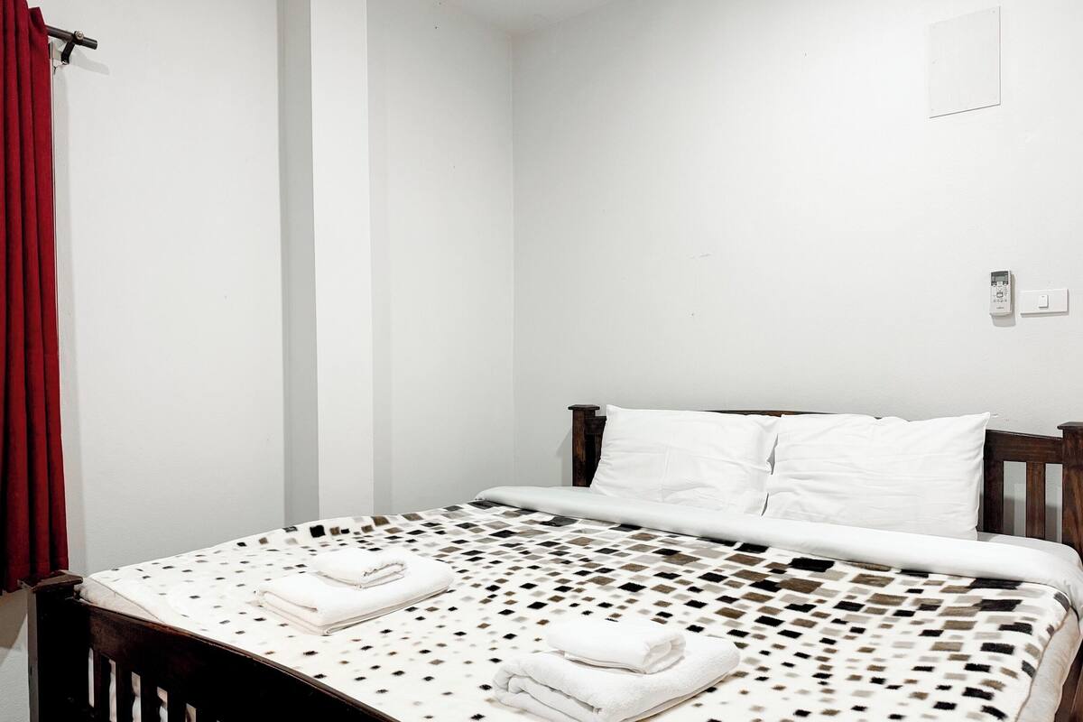 A bedroom with a bed, white pillows, and a red curtain.
