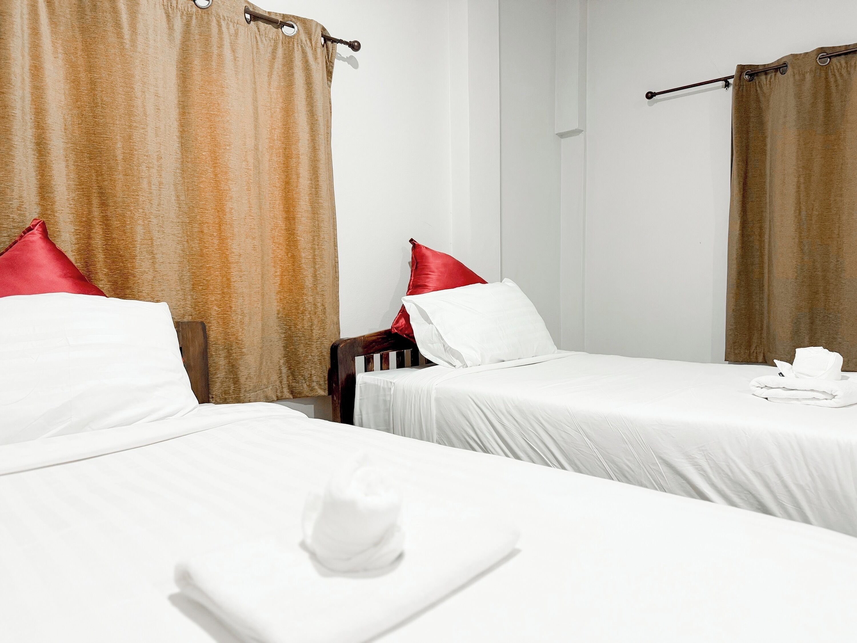 Two single beds with white linens and red pillows, a wooden headboard, and a folded towel on the bed.