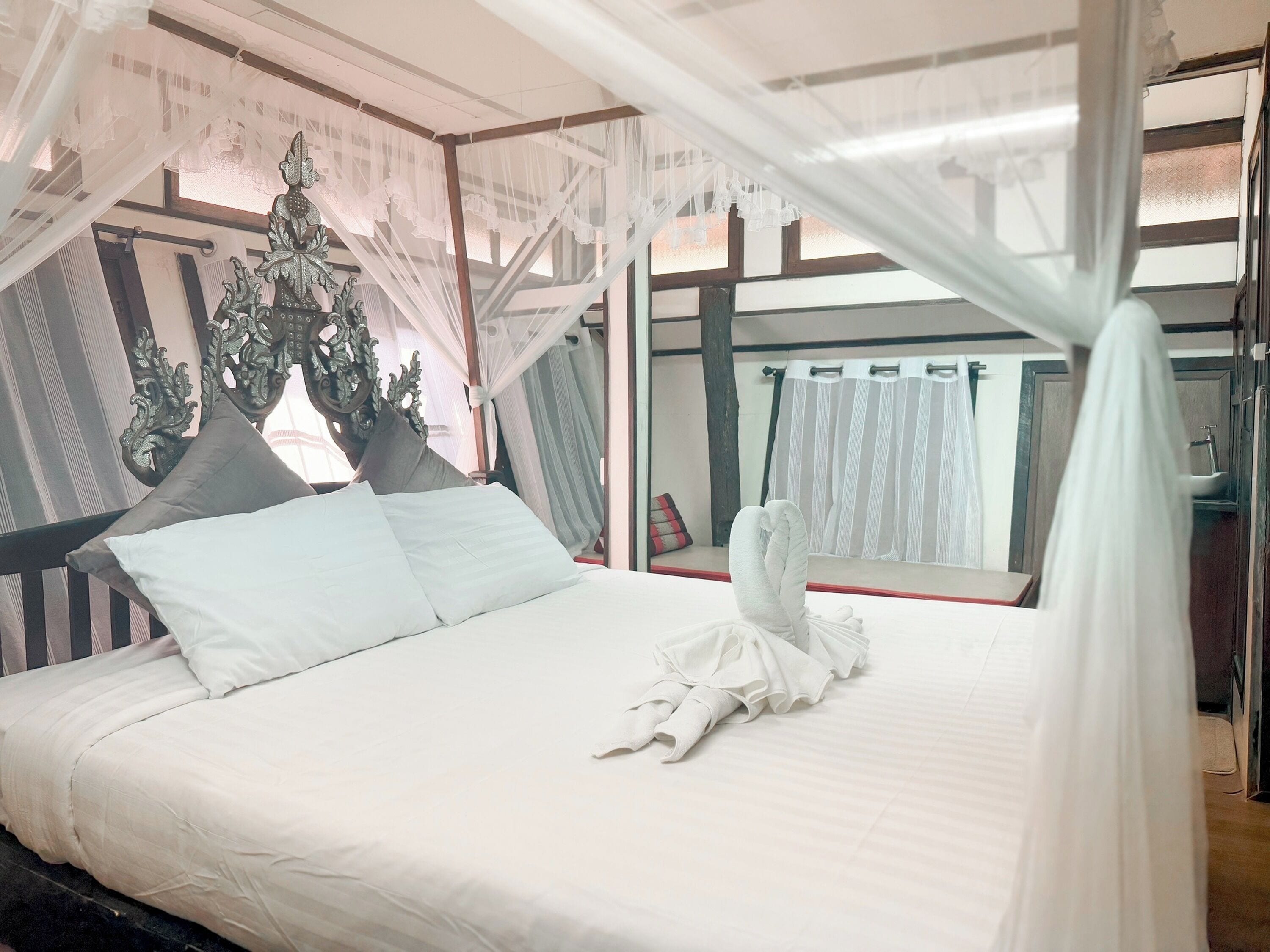A bed with white linens and a canopy, a decorative headboard, and a view of a bathroom with a sink and mirror.