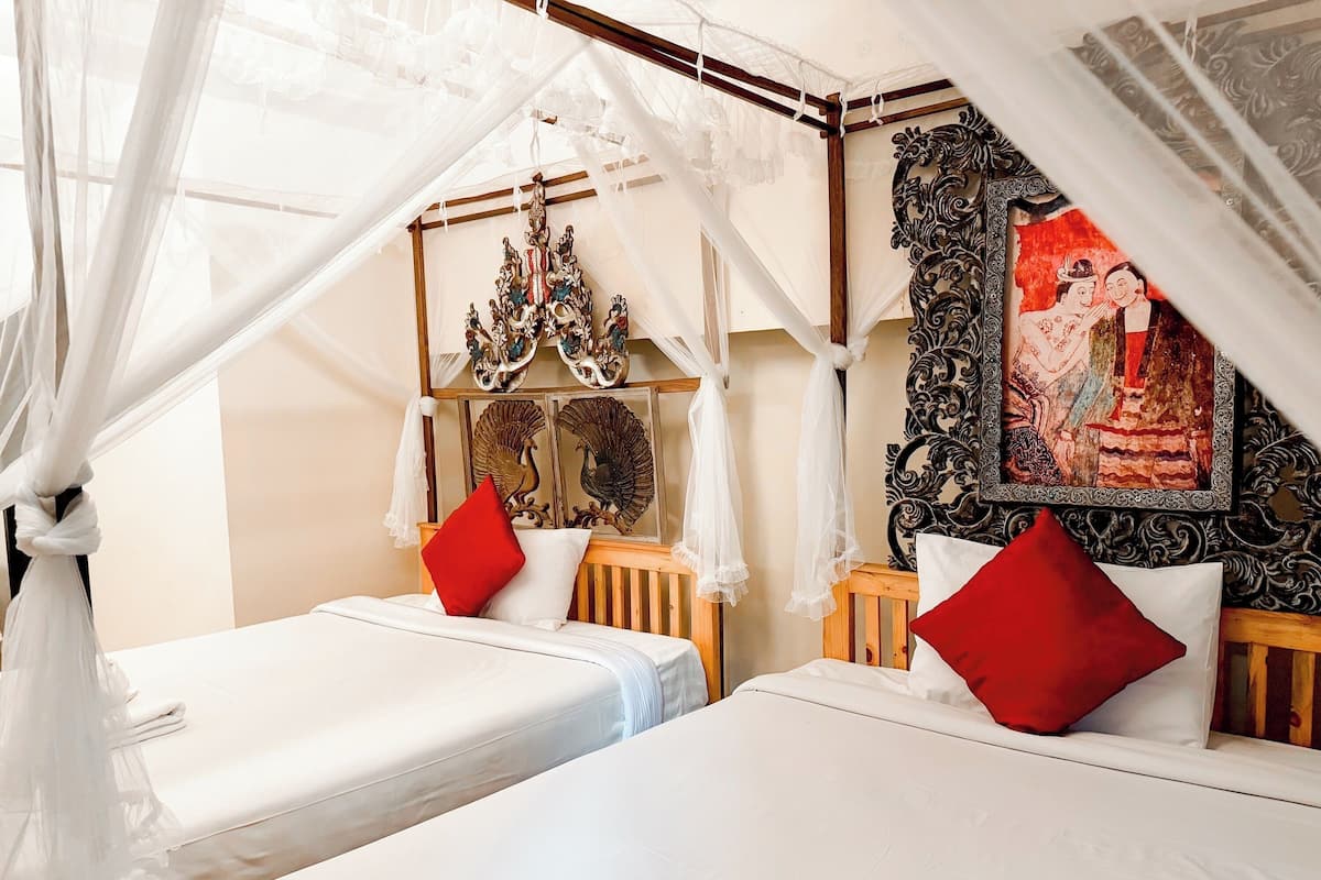 A room with two beds, a canopy bed, a decorative wall with a painting, and a ceiling with a chandelier.