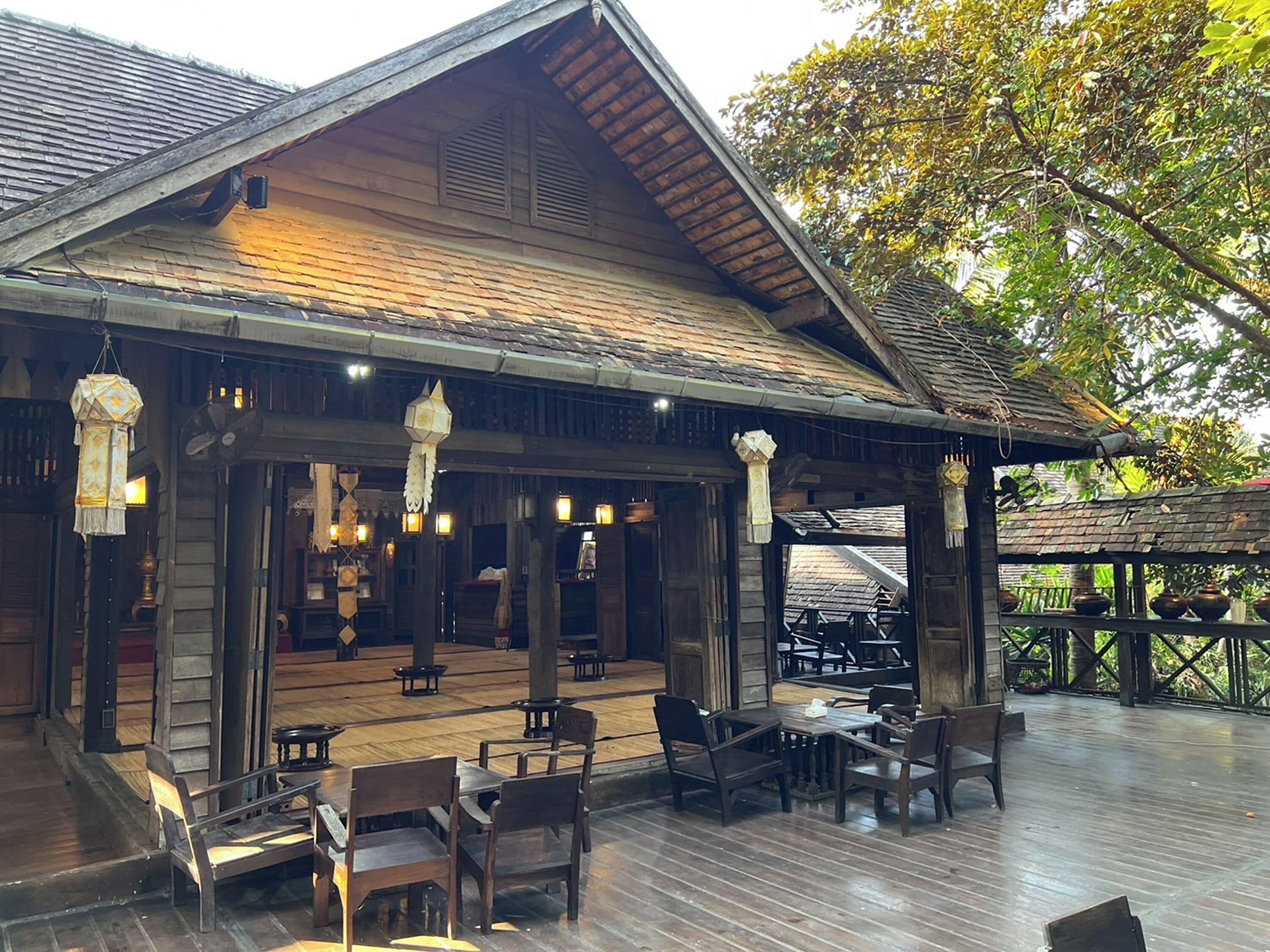 An outdoor wooden deck with tables and chairs, a covered seating area, and hanging lanterns.