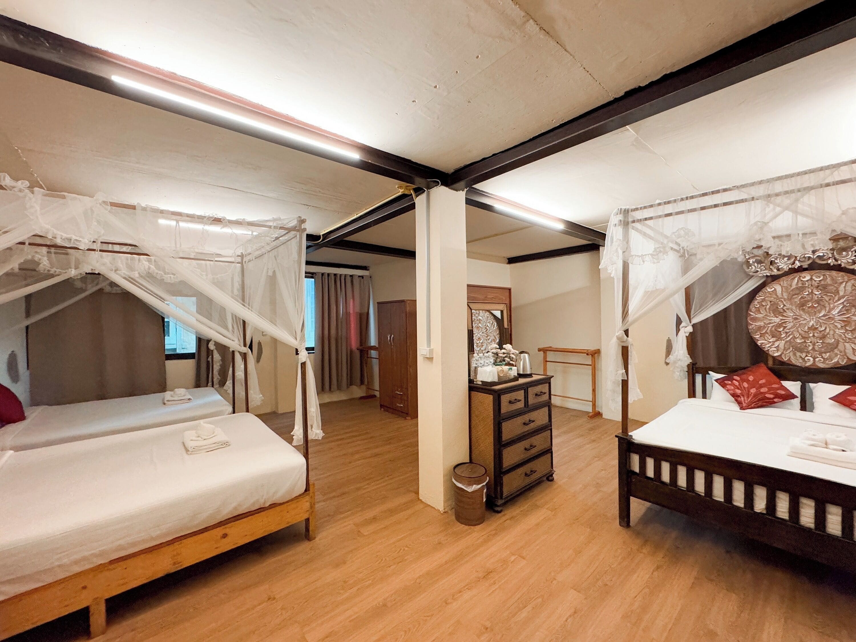 A bedroom with two beds, each with a canopy, a wooden dresser, and a mirror.