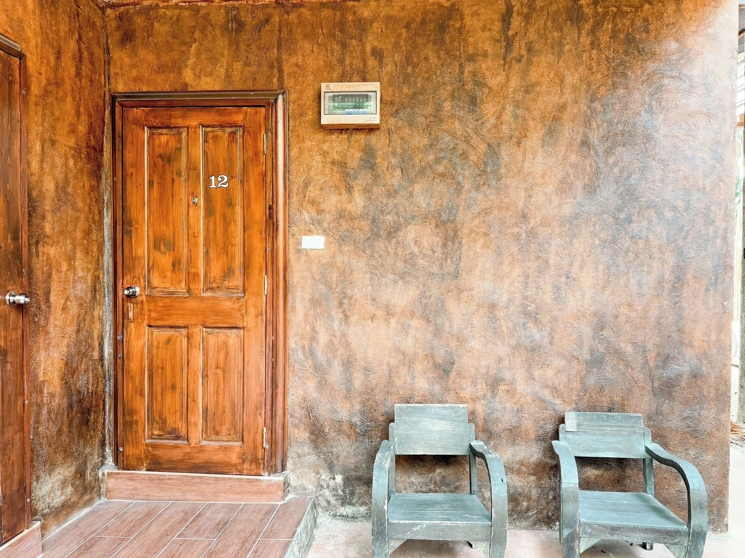 A wooden door with the number 12, two metal chairs, and a wall-mounted device.