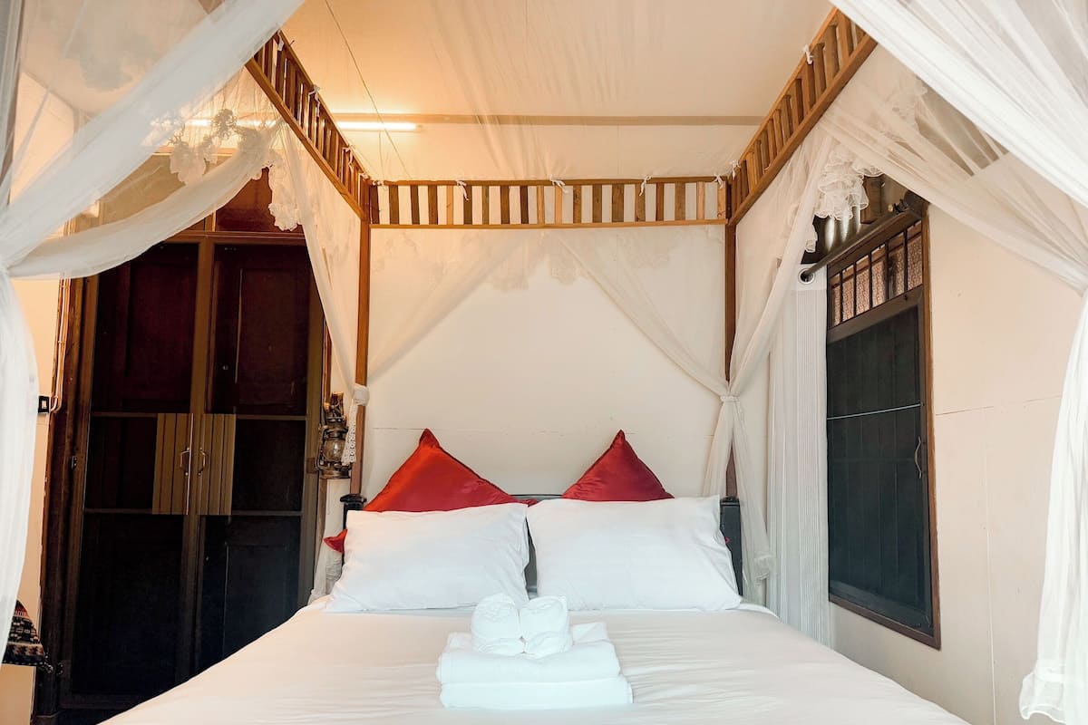 A bed with white bedding, red pillows, and a canopy.