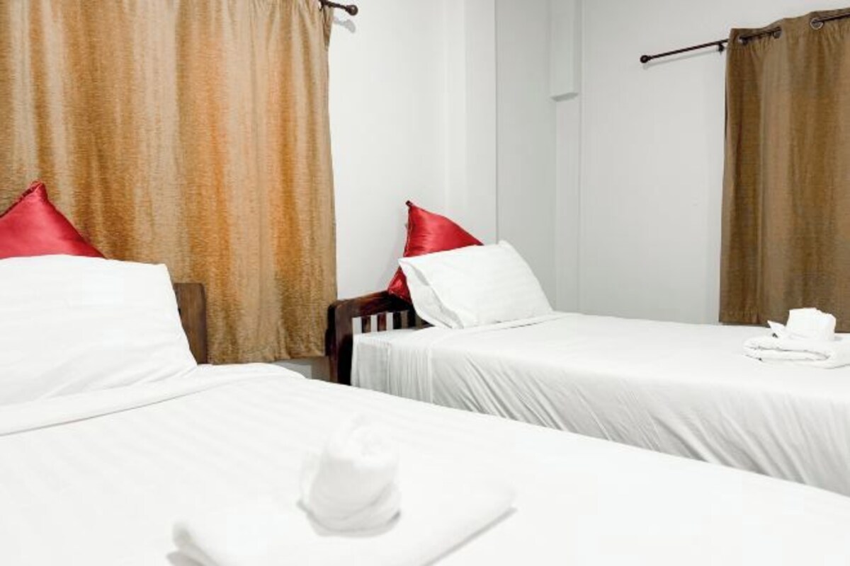 Deux lits simples avec du linge de lit blanc et des oreillers rouges, une tête de lit en bois et un rideau marron.