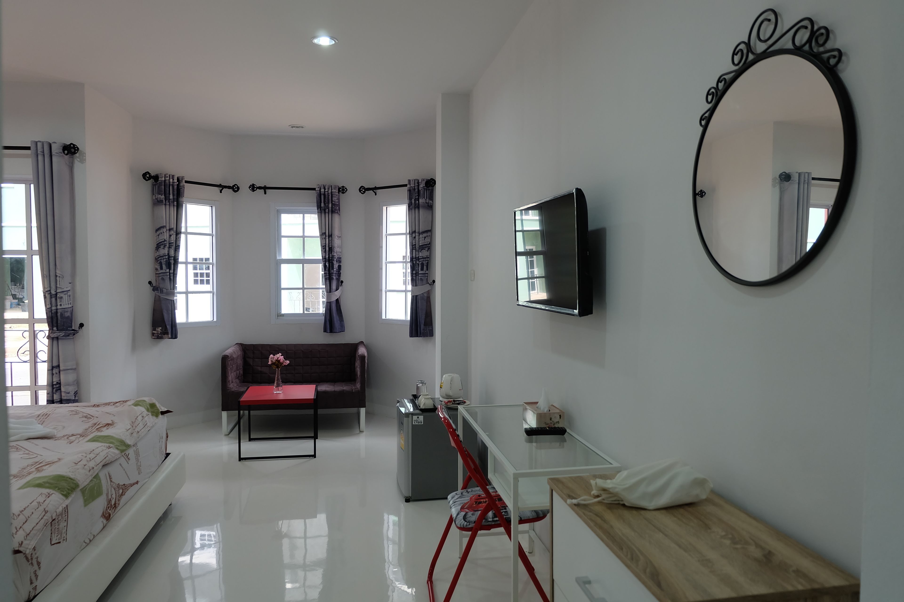 A modern hotel room with a bed, a sofa, a TV, a mirror, and a desk.