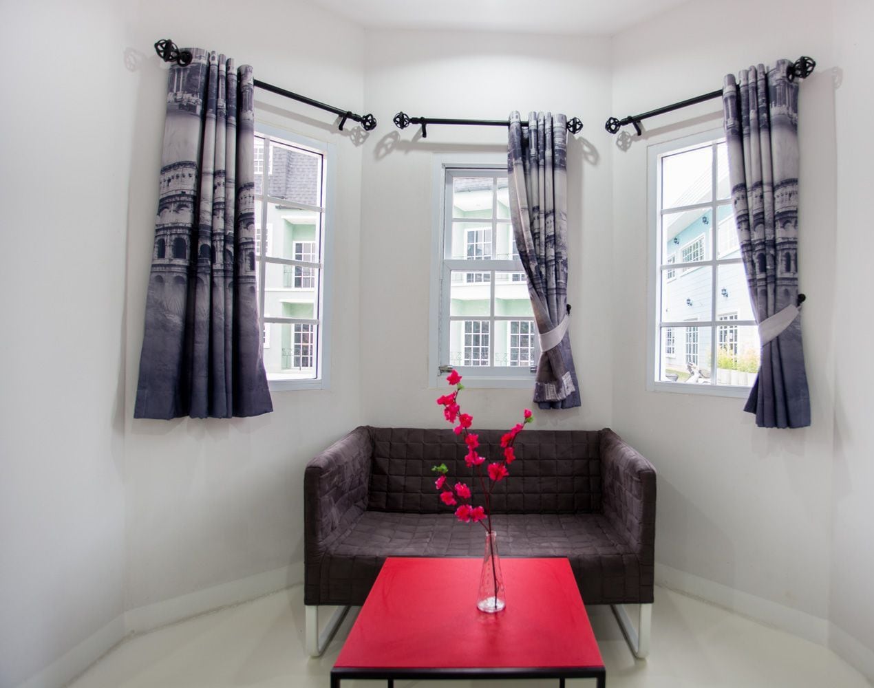 A corner room with a dark brown sofa, a red table, and a vase with pink flowers.