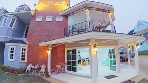 A two-story building with a brick facade, a balcony with a railing, and a covered outdoor seating area with chairs and tables.