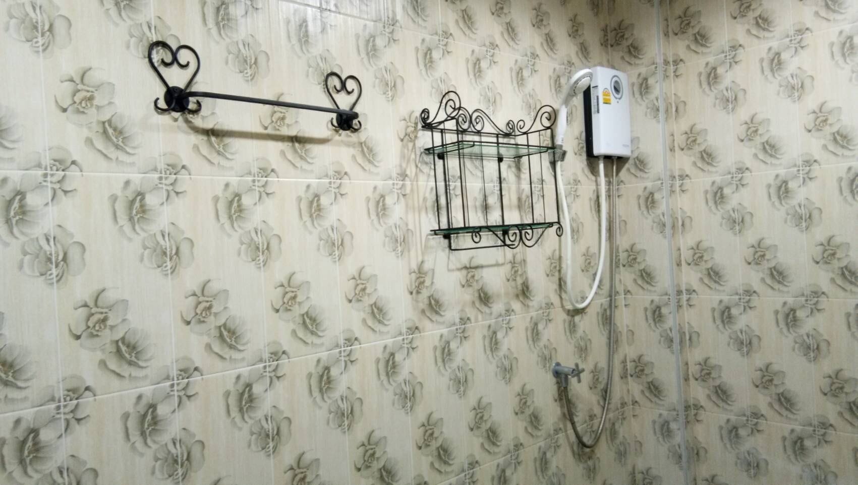 Un baño con azulejos de estampado floral, un perchero, un cabezal de ducha y un calentador de agua.