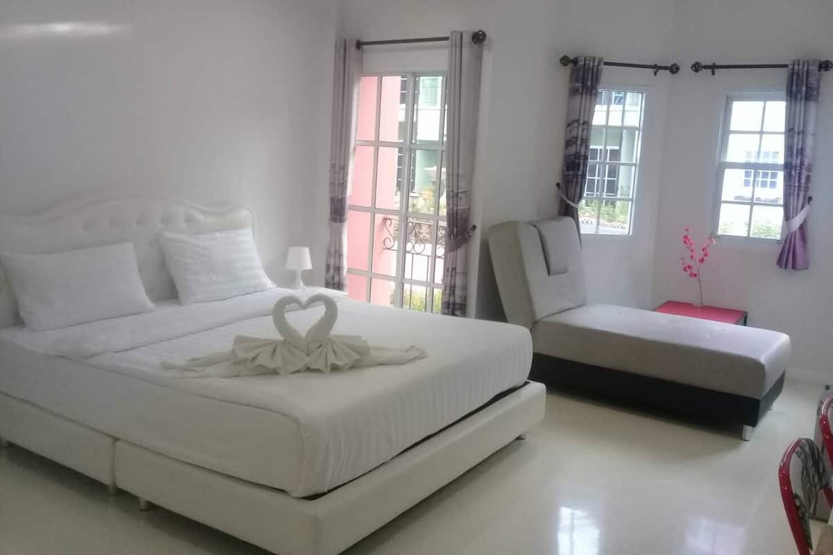 A hotel room with a large bed, a bedside table, a chair, and two windows with curtains.