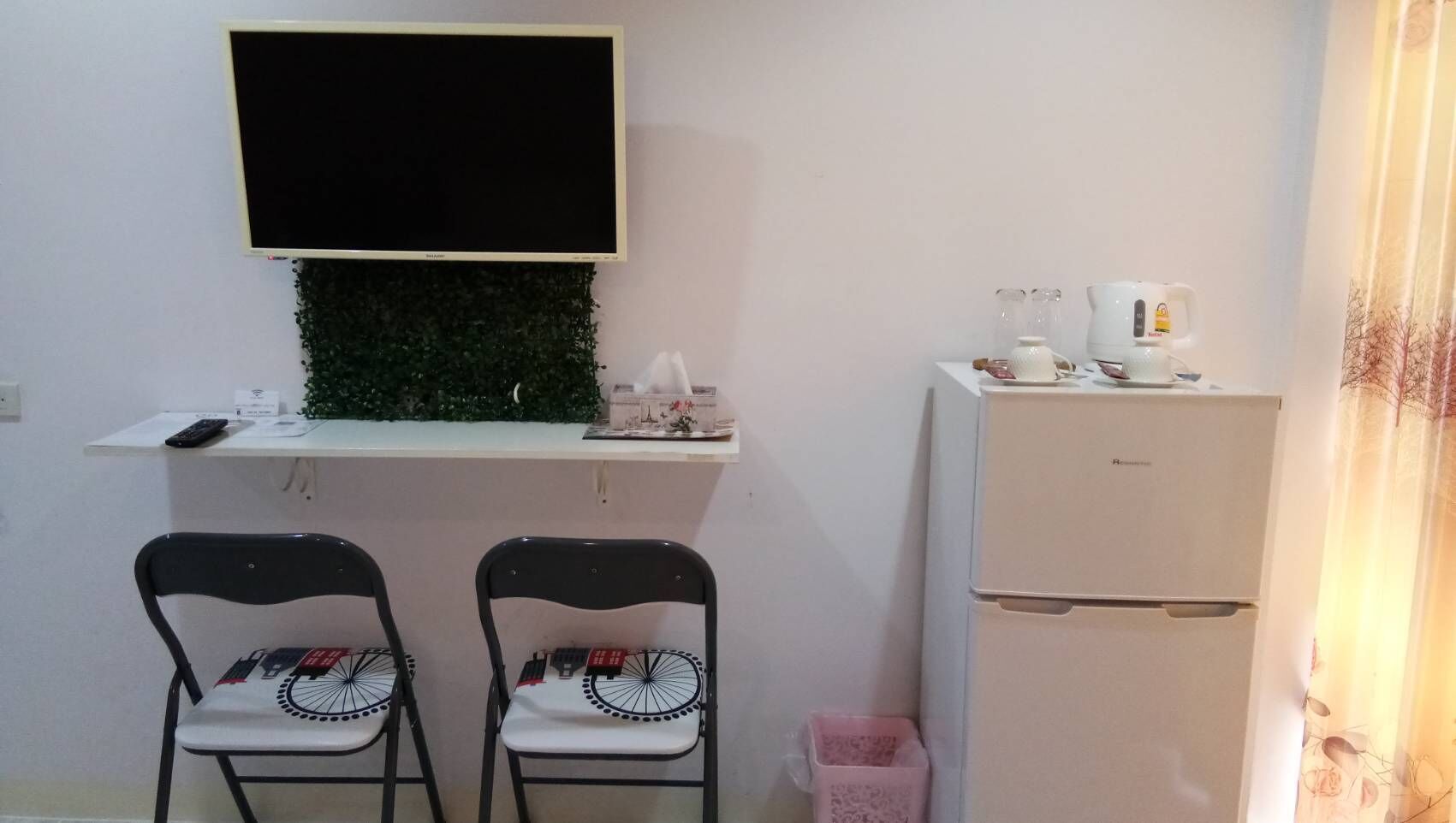 A small kitchenette with a fridge, a microwave, and a coffee maker. There are two chairs and a small table with a plant.