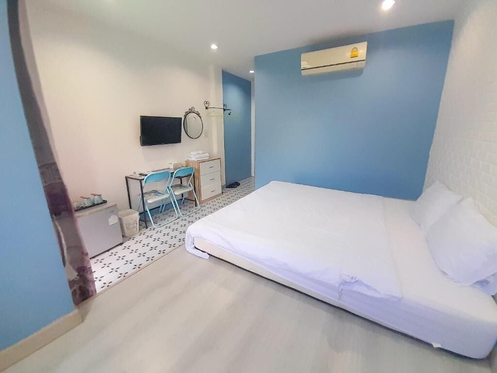 A bedroom with a bed, a desk, a chair, a TV, and an air conditioning unit.