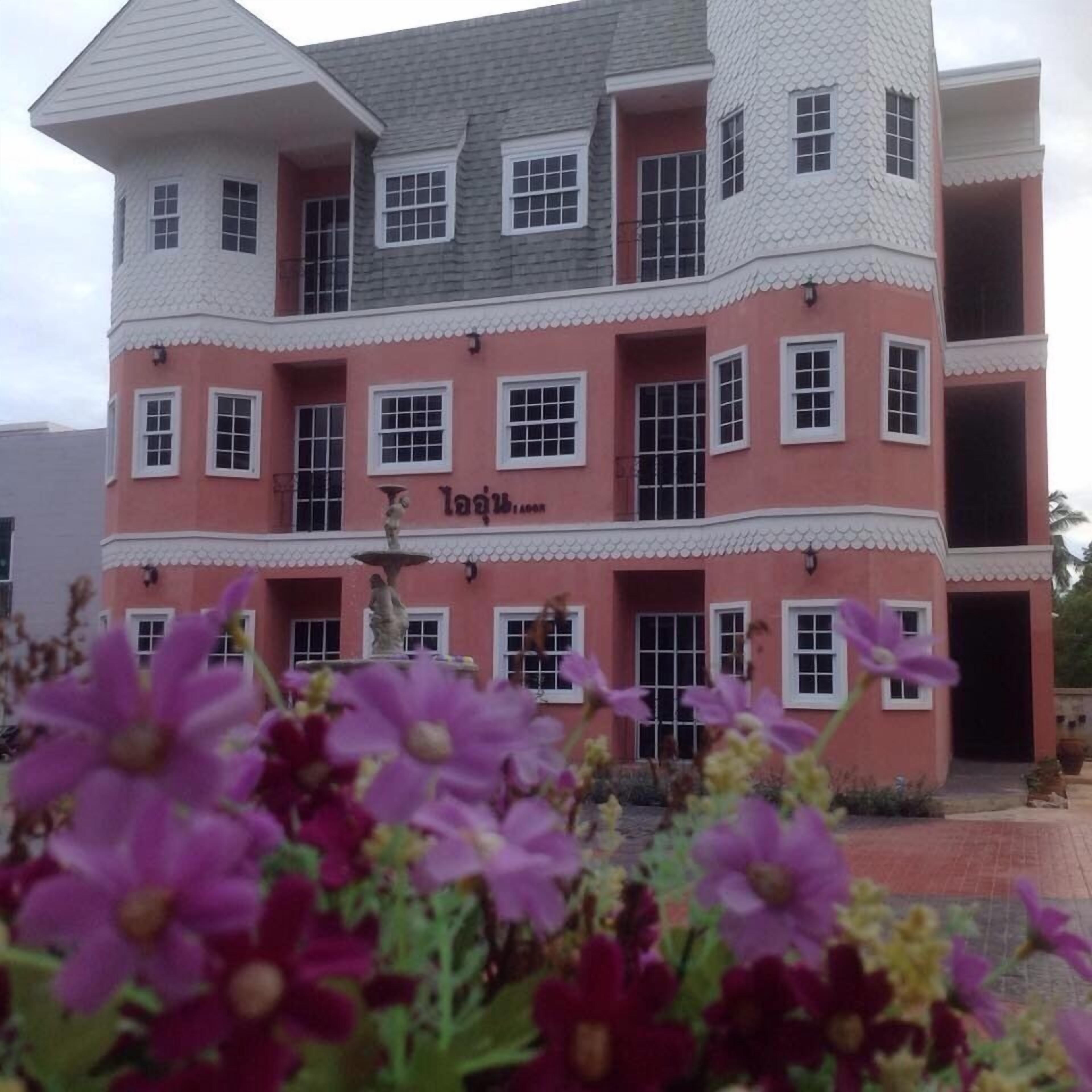 A multi-story building with a pink facade and white trim, featuring multiple windows and a central entrance.