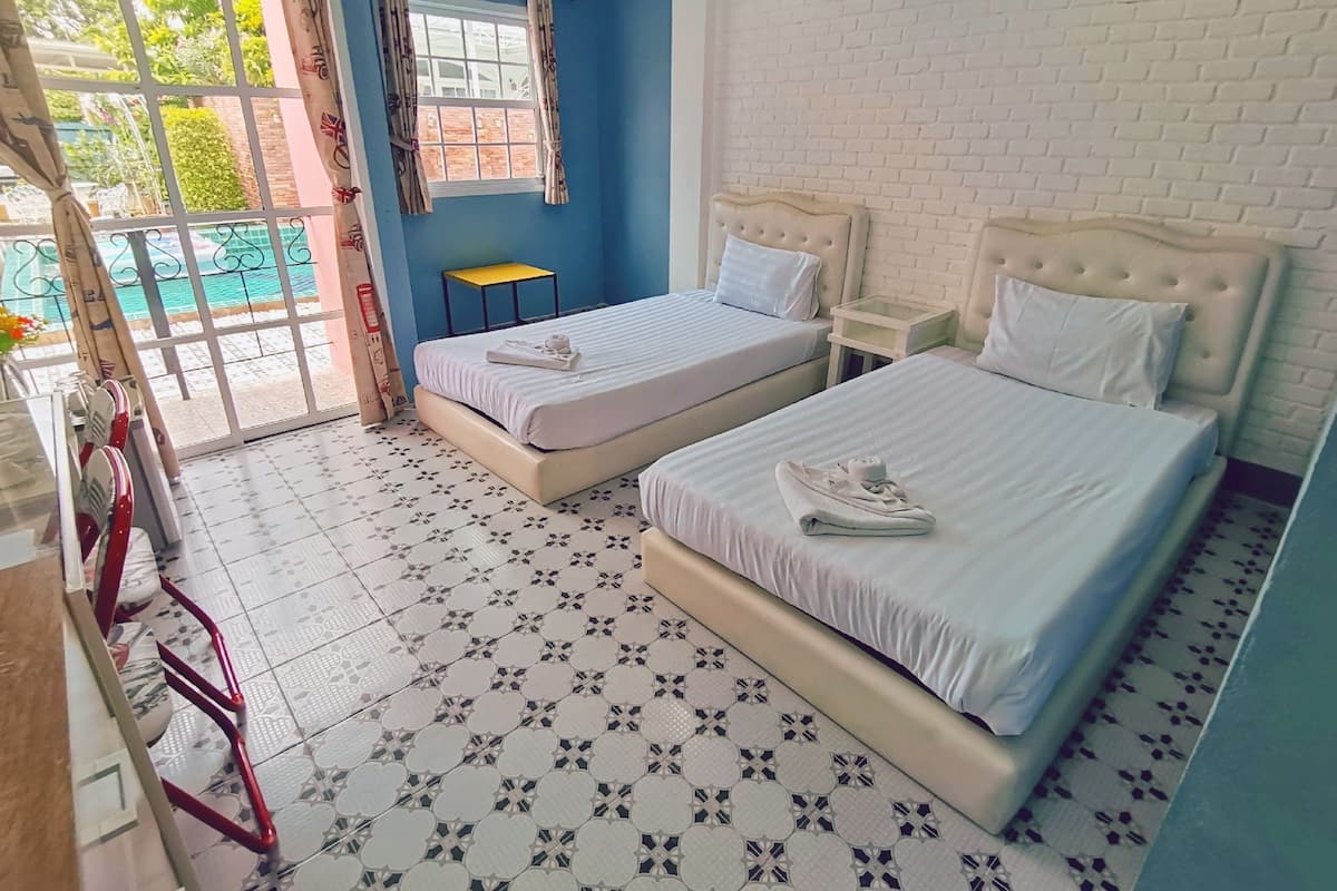 A hotel room with two beds, a small table, and a view of the outdoors.
