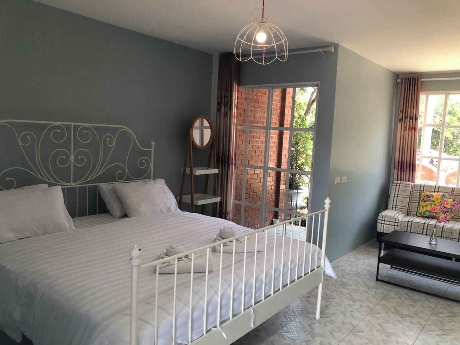 A bedroom with a bed, a hanging light fixture, a window with curtains, and a sofa.