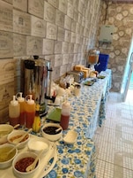 Una mesa con una variedad de alimentos y condimentos, dispuesta para un bufé, frente a una pared con diseño.