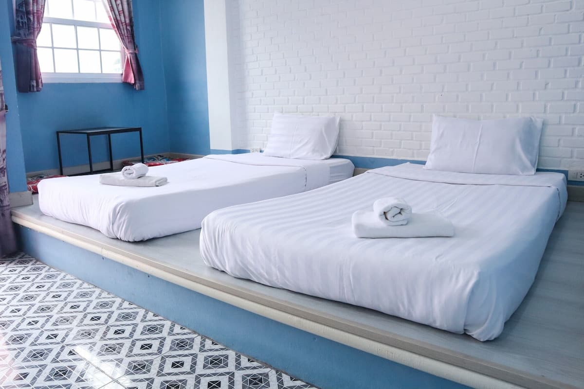 A hotel room with two beds, a window with curtains, a brick-patterned wall, and a tiled floor.