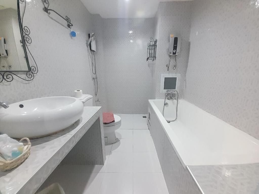 Casa de banho moderna com lavatório branco, sanita e banheira. Tem um aquecedor na parede e um pequeno armário com produtos de higiene pessoal.