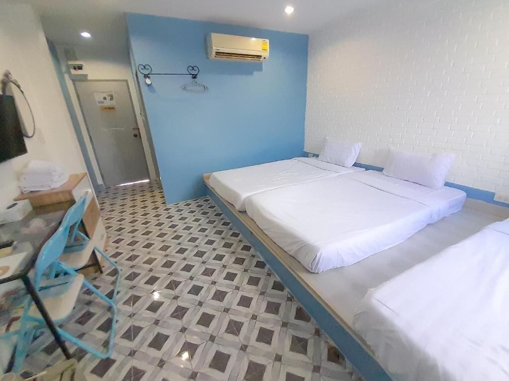 A hotel room with two beds, a desk with chairs, a tiled floor, and an air conditioning unit on the wall.