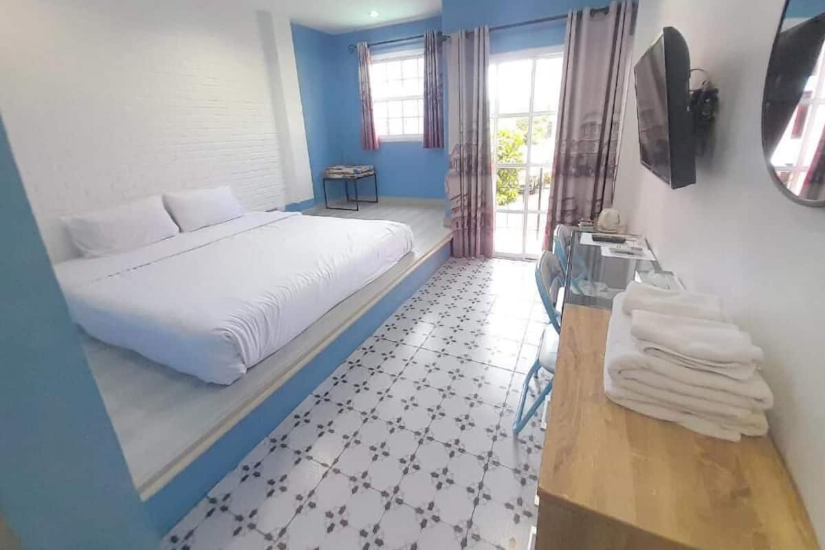 A hotel room with a large bed, a small table, a mirror, and a window with curtains.