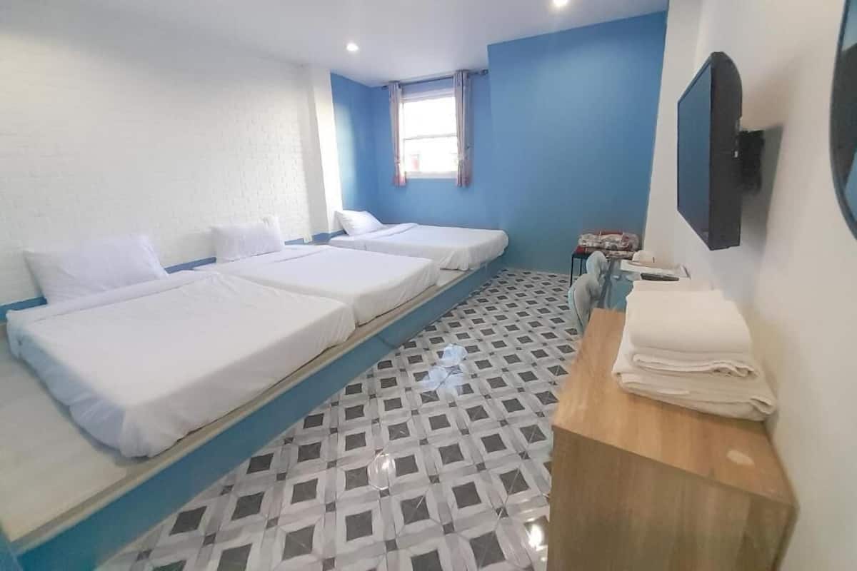 A hotel room with three single beds, a wooden desk, a mirror, and a window with curtains.