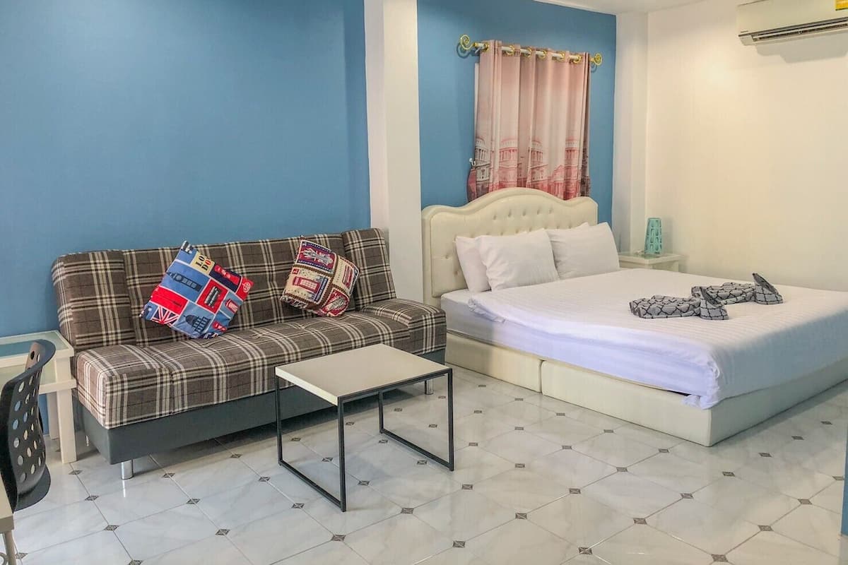 A bedroom with a bed, a sofa, a small table, and a window with curtains.