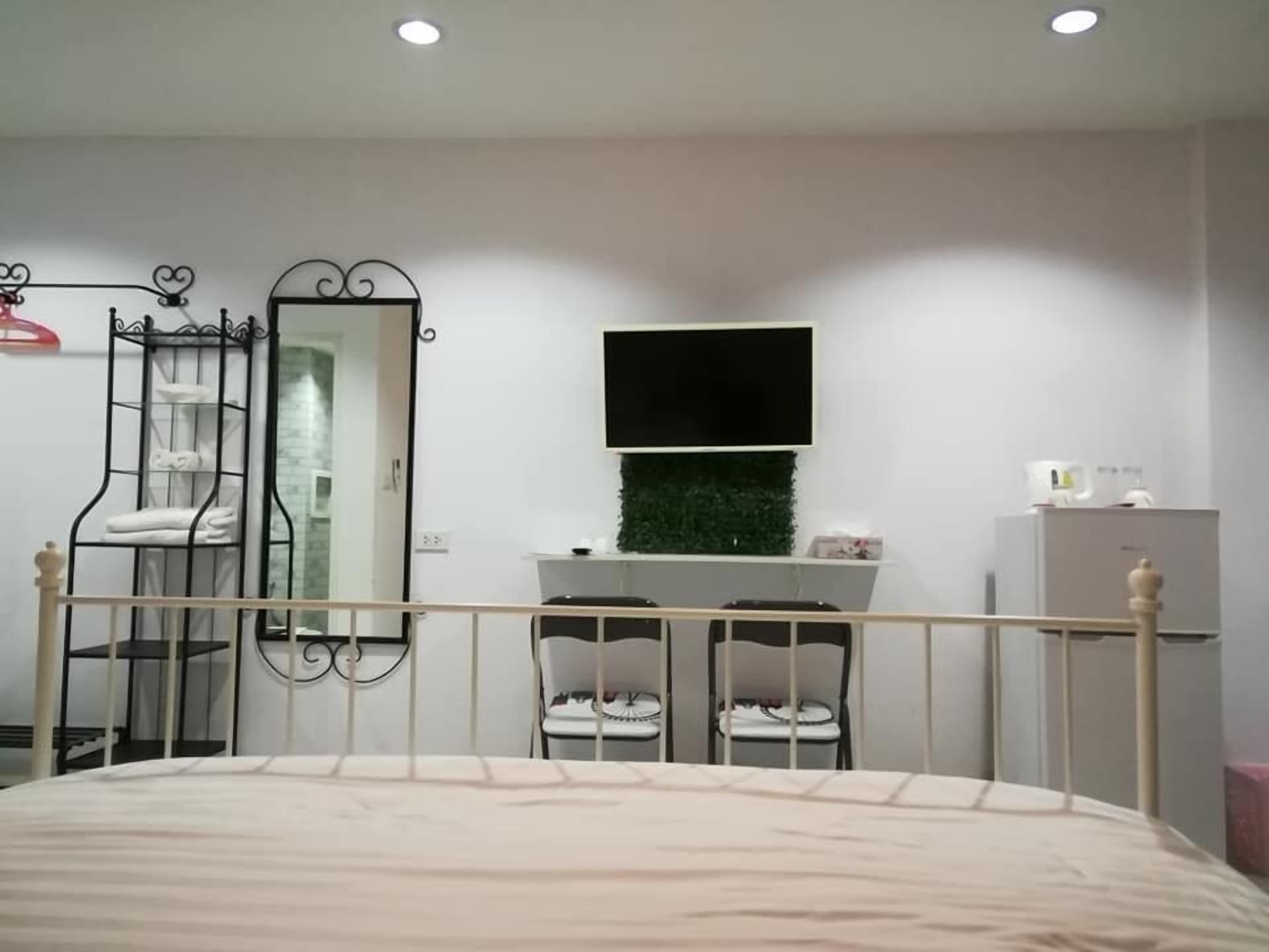 A bedroom with a bed, a wardrobe, a mirror, a television, and a small seating area.