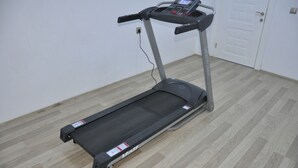 A treadmill in a room with wooden flooring and a white door in the background. - Ozyigit Otel (Gazipasa)