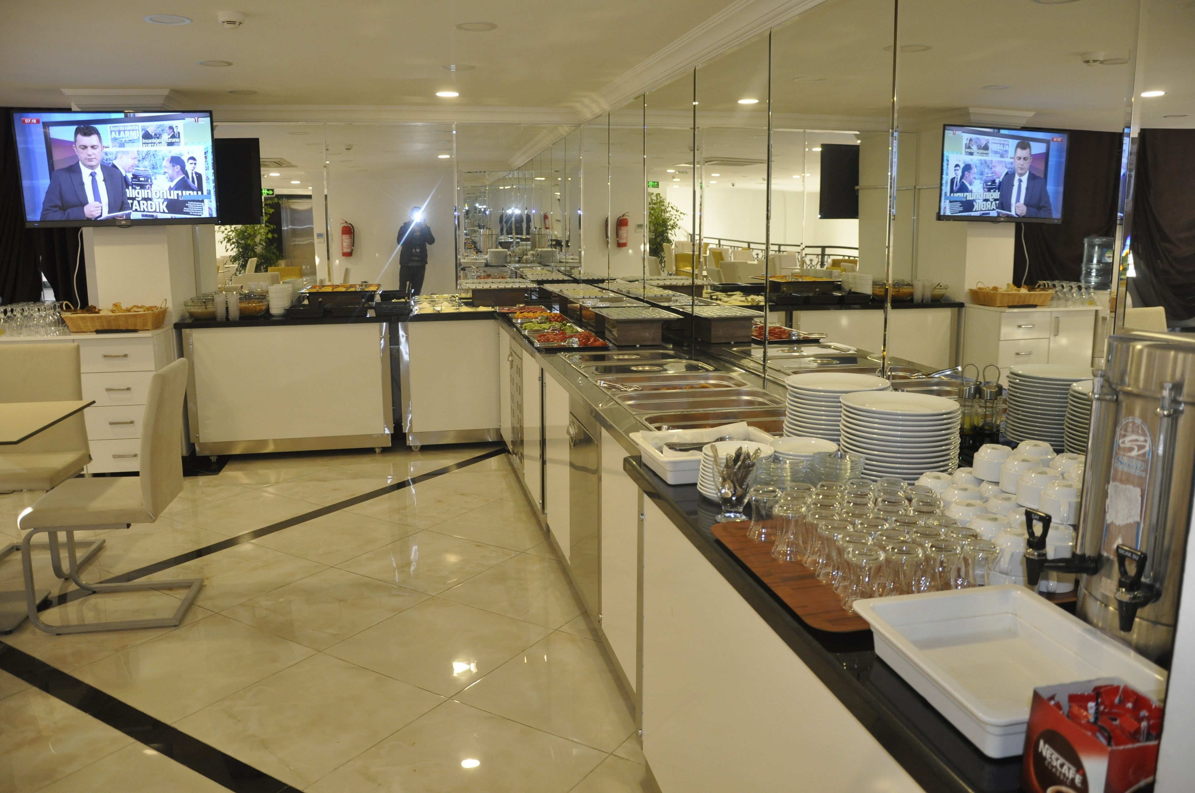 A buffet area with multiple serving stations, a television mounted on the wall, and a person walking in the background.