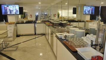A buffet area with multiple serving stations, a television mounted on the wall, and a person walking in the background.