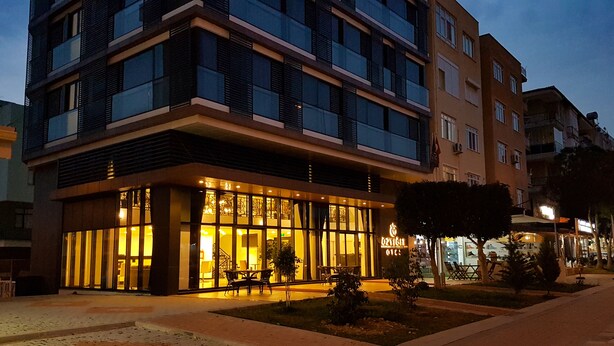 A modern hotel with a glass facade, outdoor seating, and a well-lit entrance. - Ozyigit Otel (Gazipasa)