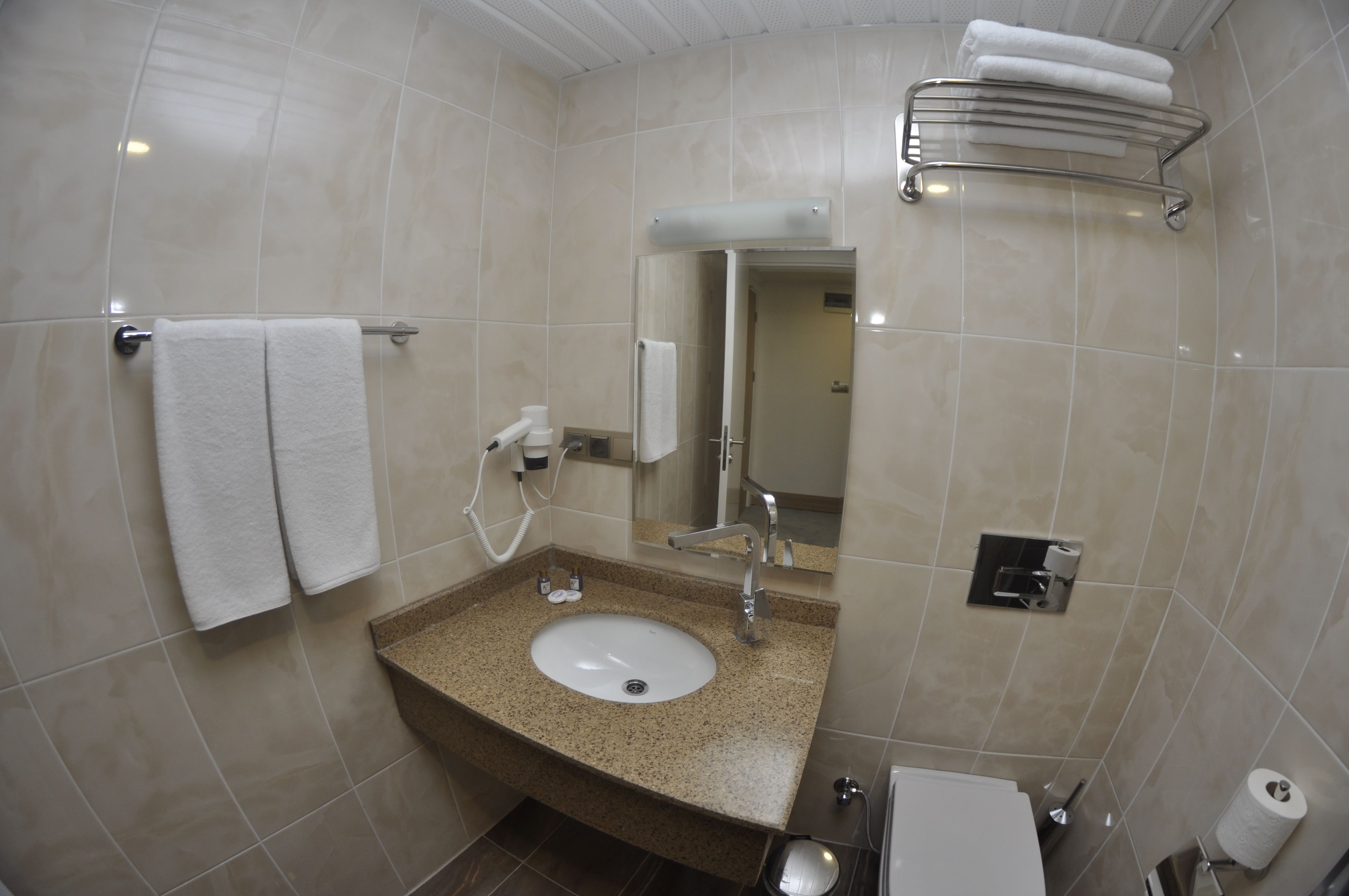 Un baño con lavamanos, espejo, toallero y retrete.