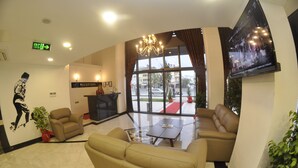 A hotel lobby with a reception desk, sofas, a chandelier, and a large window offering a view of the outside. - Ozyigit Otel (Gazipasa)