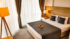 A hotel room with a large bed, two bedside tables, a nightstand, a lamp, and a window with curtains. - Ozyigit Otel (Gazipasa)
