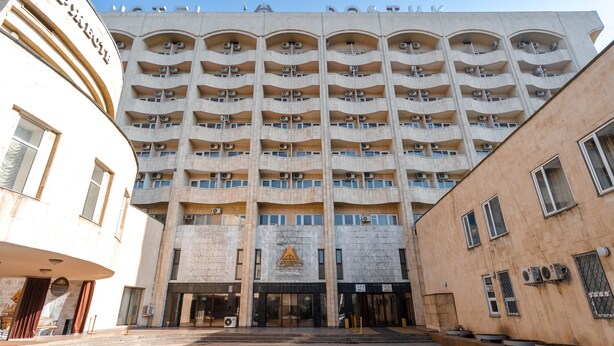 Un hotel a più piani con un ingresso centrale, balconi e condizionatori.