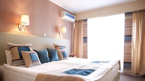 Una camera d'albergo con un letto grande, due lampade a parete, un condizionatore d'aria e una finestra con tende.