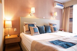 A hotel room with a neatly made bed, two bedside lamps, an air conditioning unit, and a window with curtains. - Club Hotel Dostuk (Bishkek)