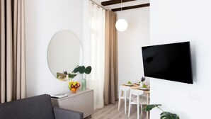 A modern living room with a grey sofa, a round mirror, a dining table with chairs, and a mounted TV. - Apartamentos Wallace Valencia (Valencia)