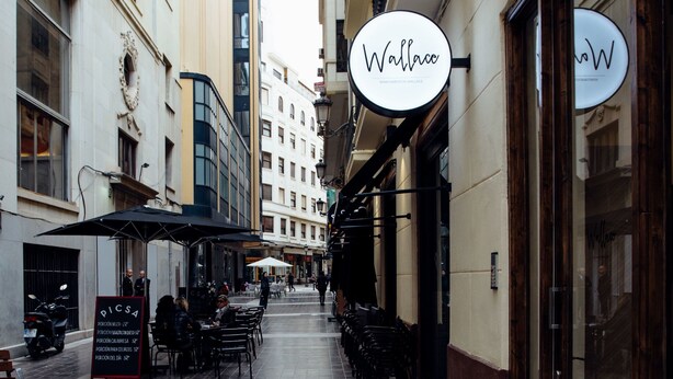 A narrow street with outdoor seating, a cafe named "Wallace," and a building with large windows. - Apartamentos Wallace Valencia (Valencia)