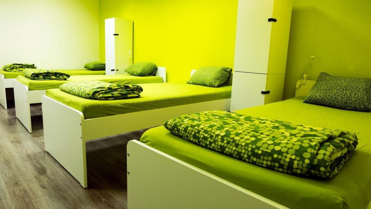 Quarto com três camas, cada uma com roupa de cama e almofadas verdes.