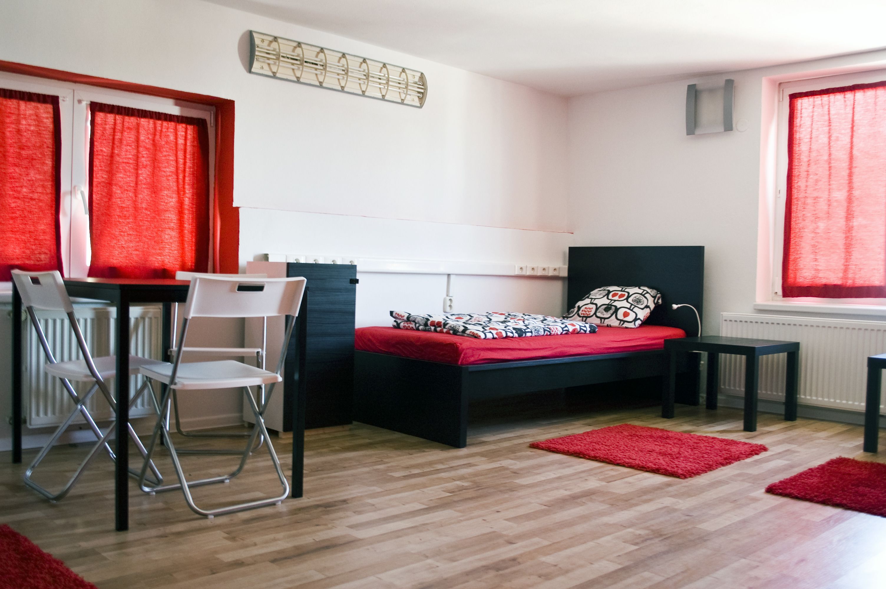 A small, modern bedroom with a bed, a desk, and two chairs.