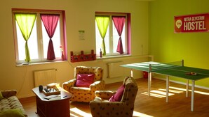 Una habitación con mesa de ping pong, dos sillones, una pequeña mesa con piezas de ajedrez y un cartel que indica que es un albergue.