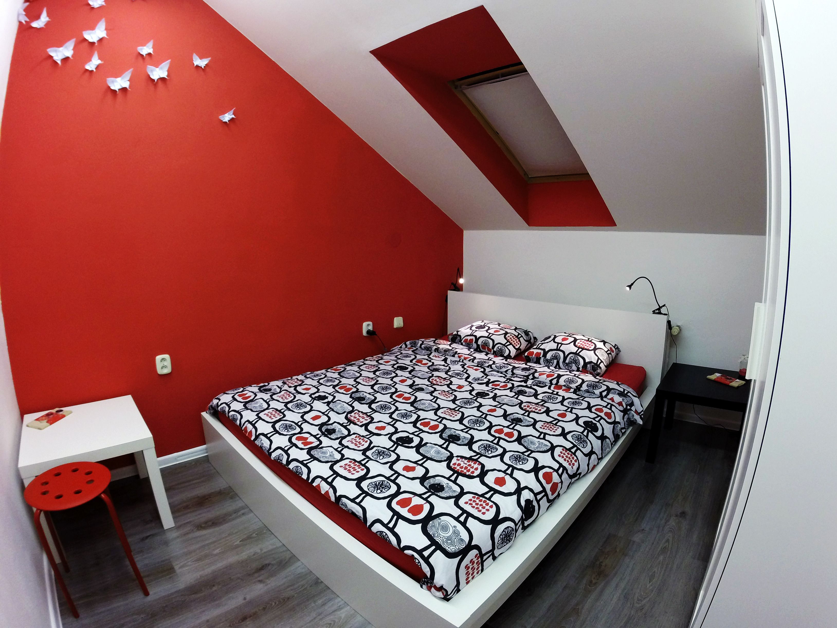 Ein Schlafzimmer mit schrägverdachter Decke, einem Bett mit gemusterten Textilien, einem Schreibtisch und einem Stuhl.