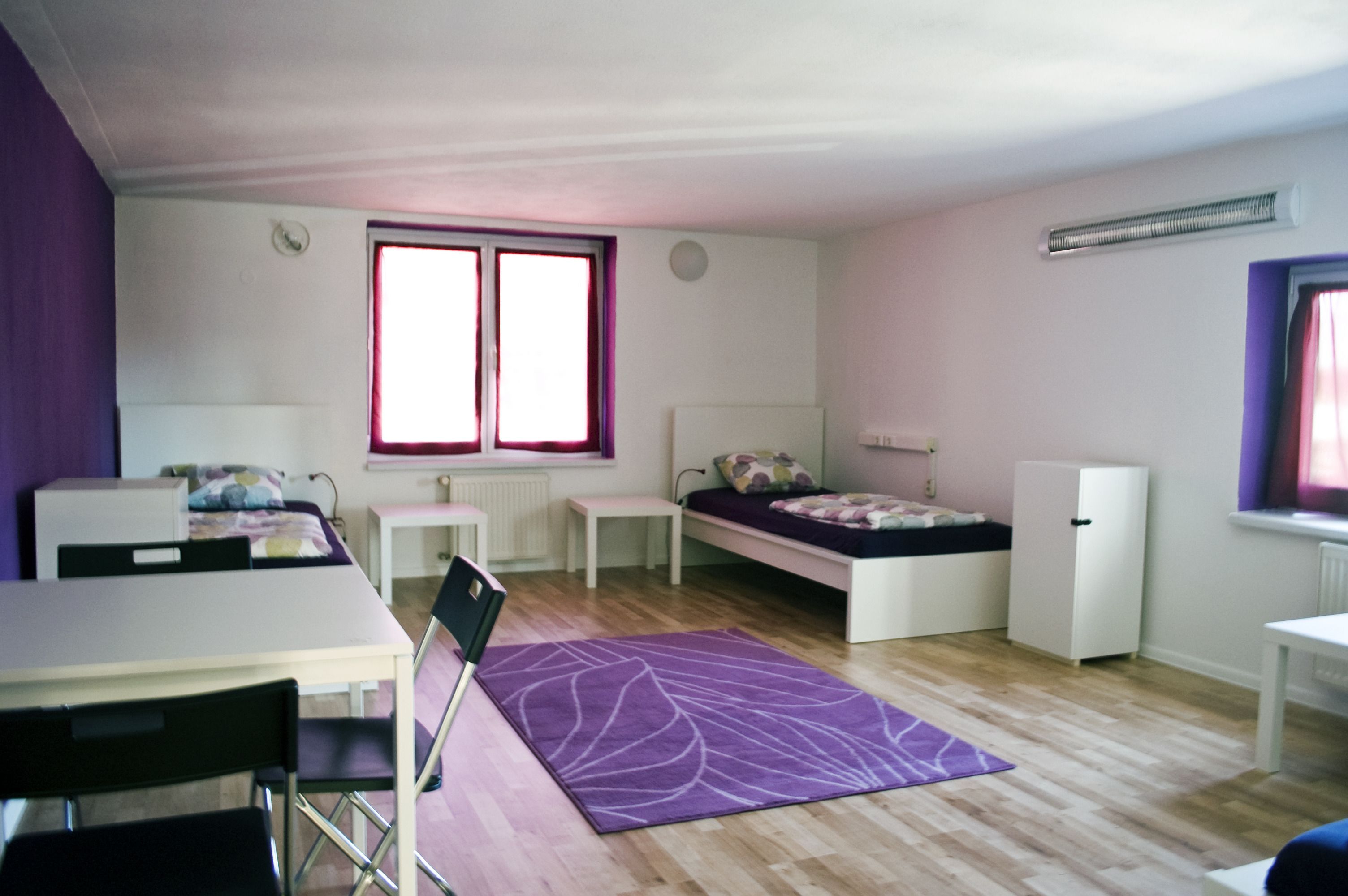 Une petite pièce comprenant un lit, un bureau, une chaise, une petite table et un radiateur.