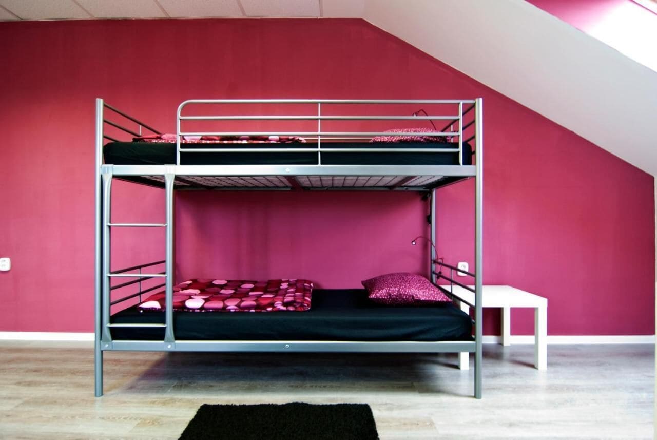 Een stapelbed met een witte tafel ernaast, voor een rode muur in een kamer met een schuine plafond.