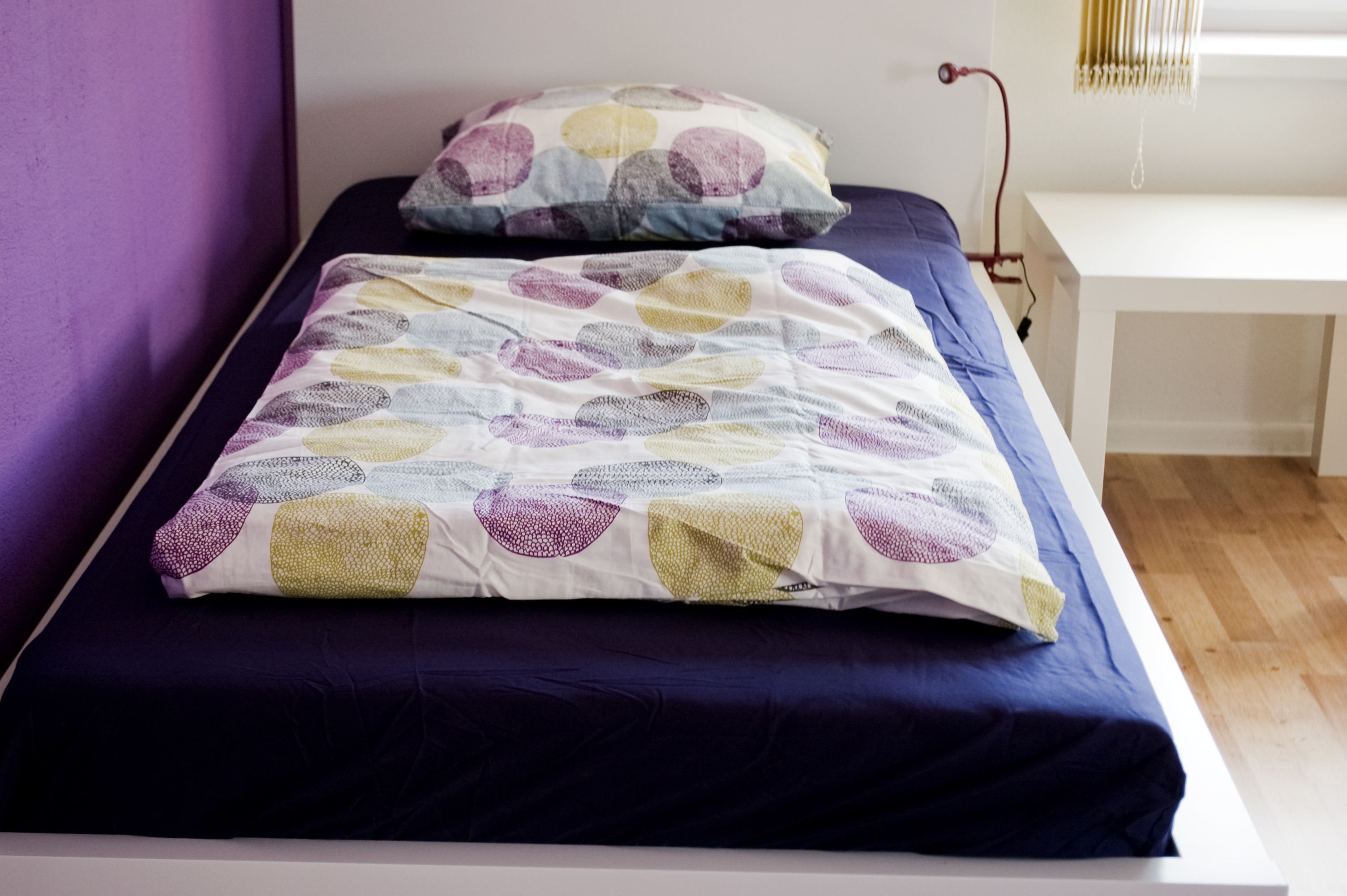 A bed with a patterned bedspread and pillows, a bedside table, and a lamp.